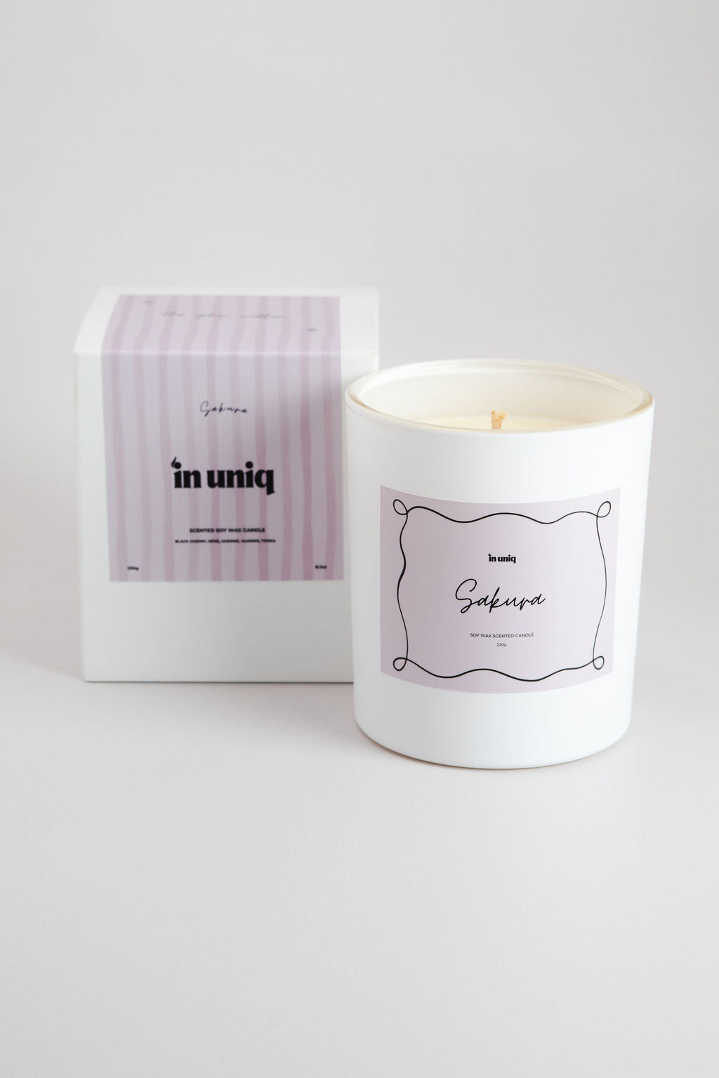 A white glass jar candle with a lavender label next to its white and lavender striped packaging box, on a light gray background.