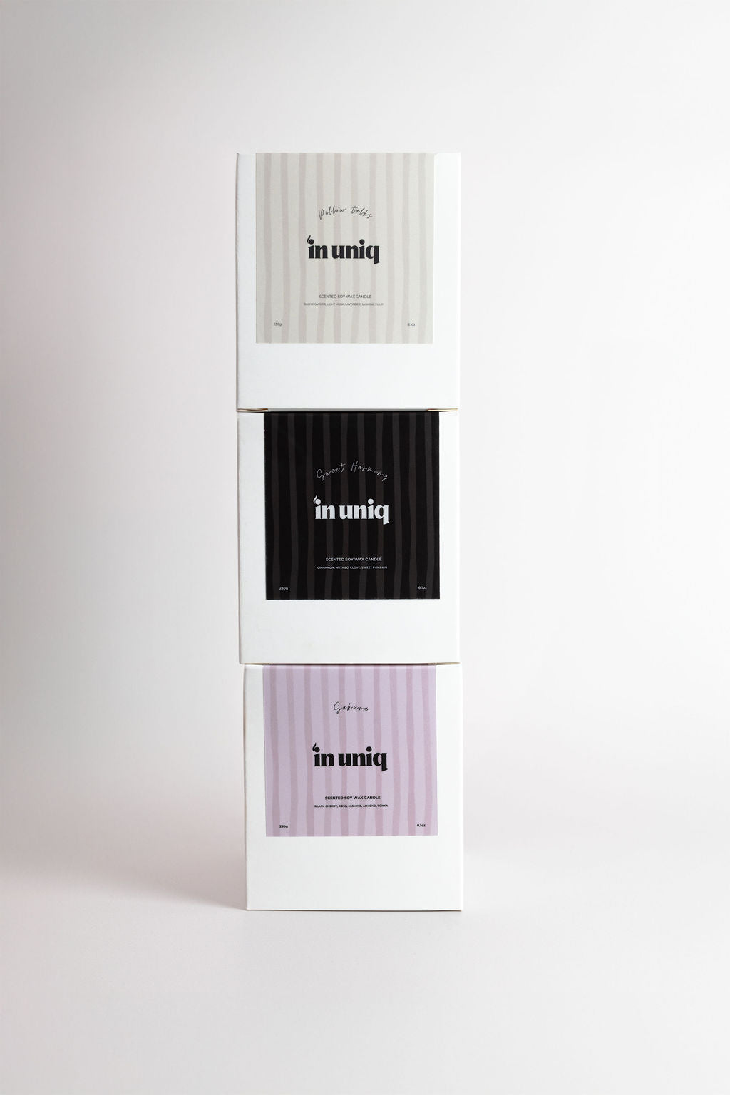 Three stacked rectangular product boxes on a light gray background, each with a white label area showing the text 'in uniq' and different stripe patterns: light gray, black, and pale lavender.